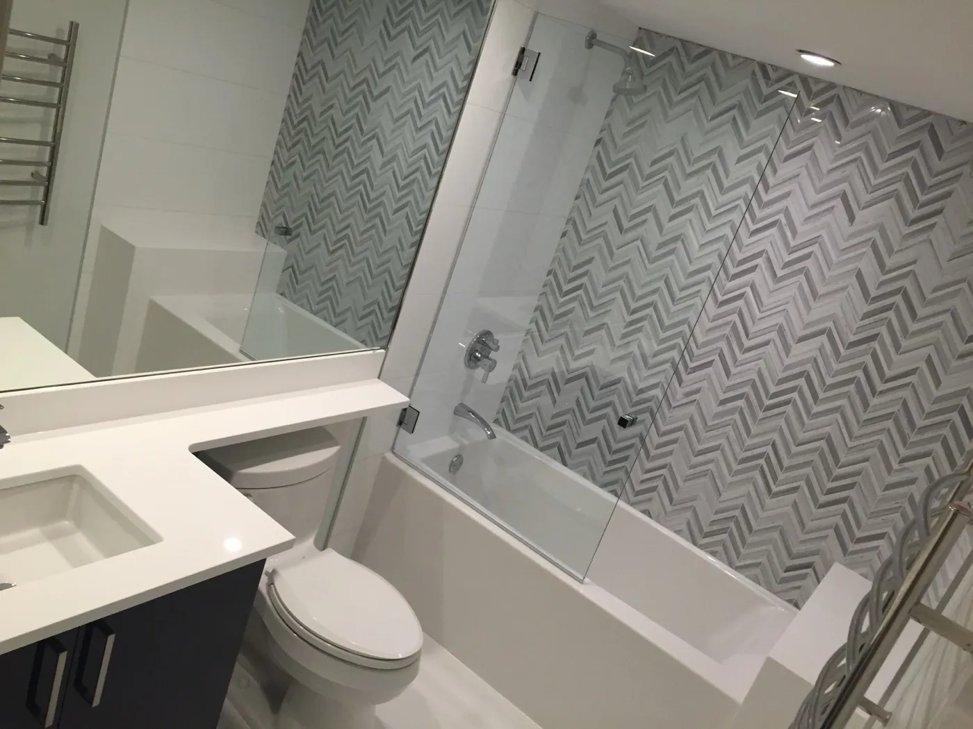 Bath with a grey chevron mosaic feature wall, white quartz vanity, and heated towel rail