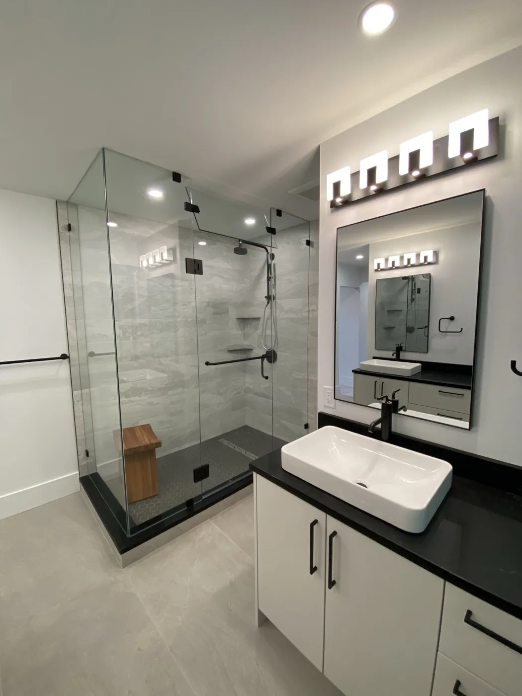 Modern grey bath with a glass walk-in shower, teak bench, and backlit mirror