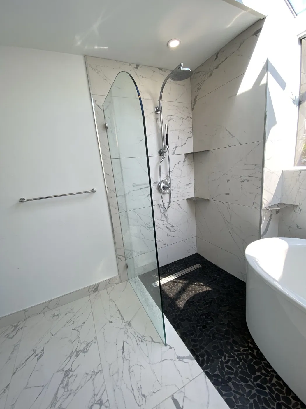 Walk-in marble shower with a frameless glass screen and black pebble floor