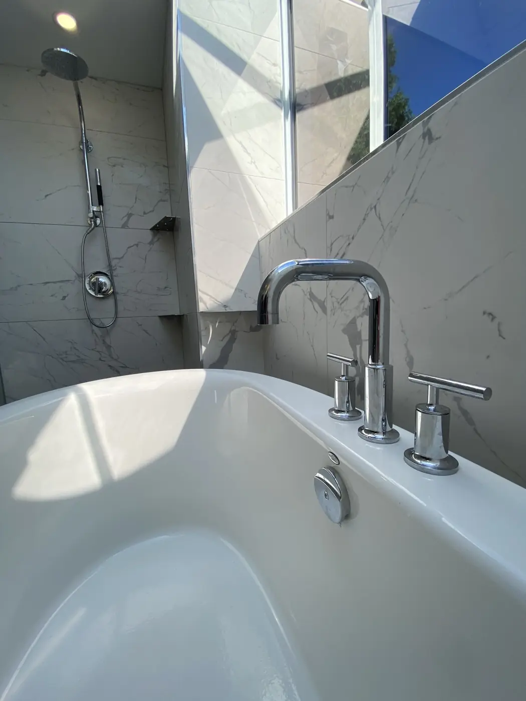 Freestanding tub with chrome fixtures against marble walls in a renovated primary bath