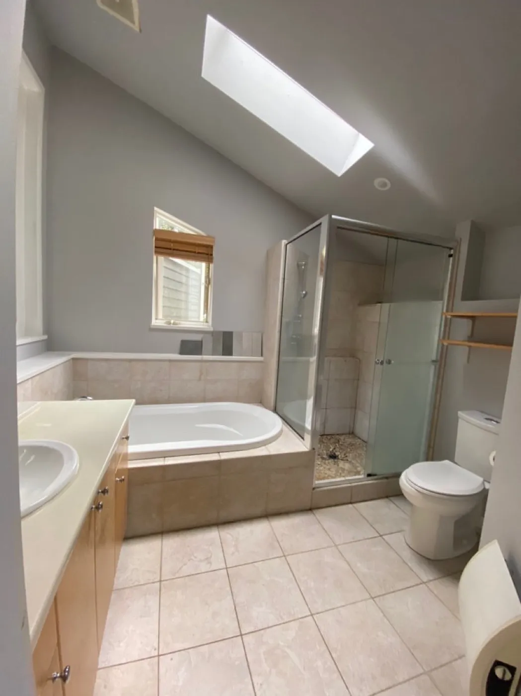 Dated primary ensuite before renovation, with cream tile, an oak vanity, and a boxed-in corner tub